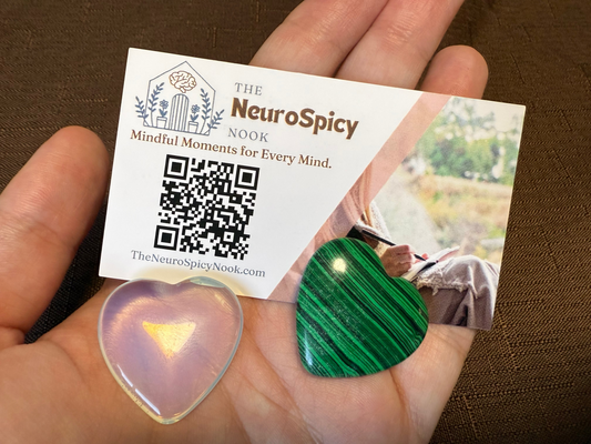 Hand holding a NeuroSpicy business card with a QR code and worry stones.